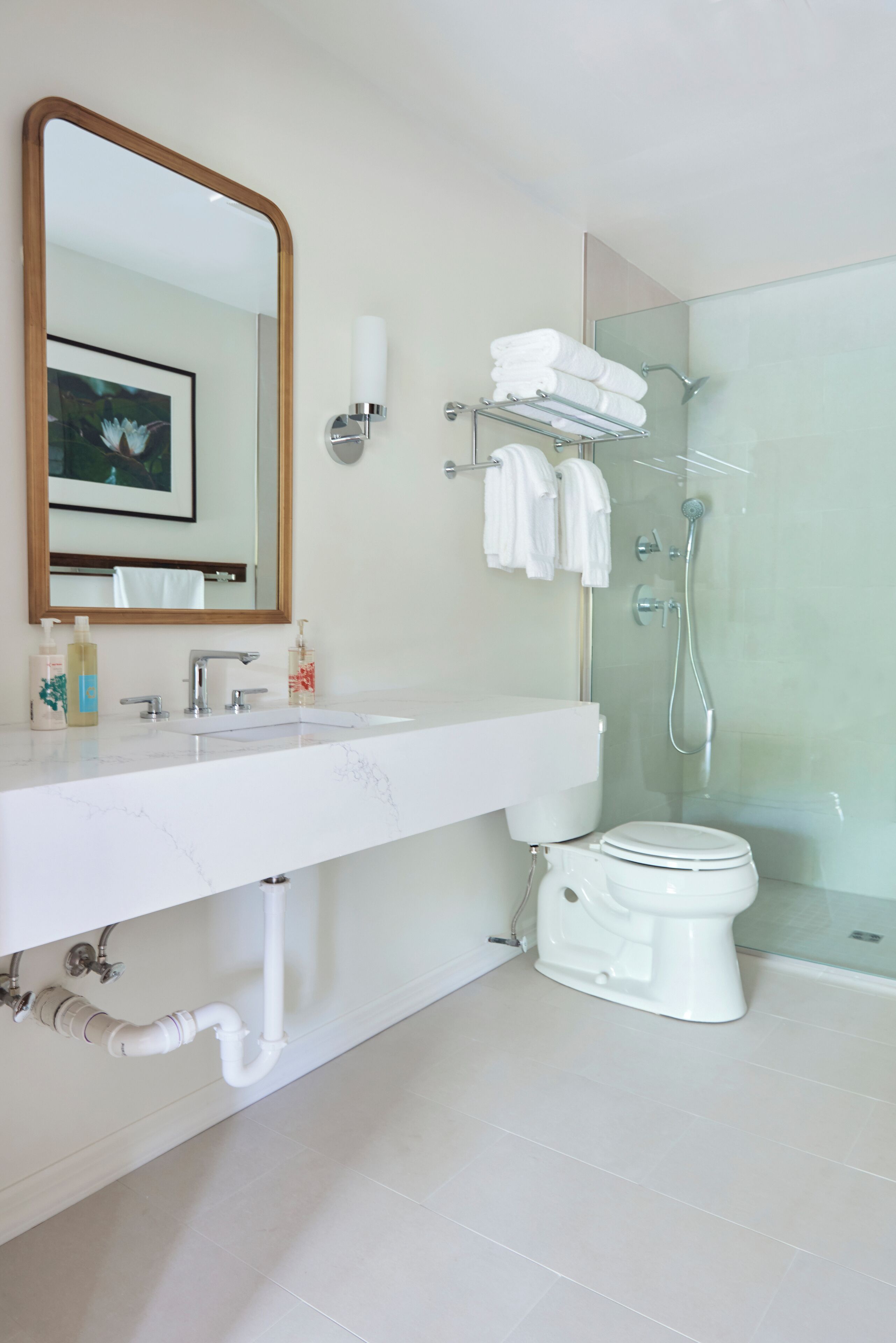 Een moderne badkamer met een witte wastafel, spiegel en toilet. Er is een douchecabine met glazen wanden en een handdoekrek met handdoeken.