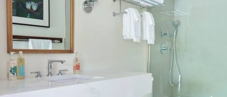 Een moderne badkamer met een witte wastafel, spiegel en toilet. Er is een douchecabine met glazen wanden en een handdoekrek met handdoeken.