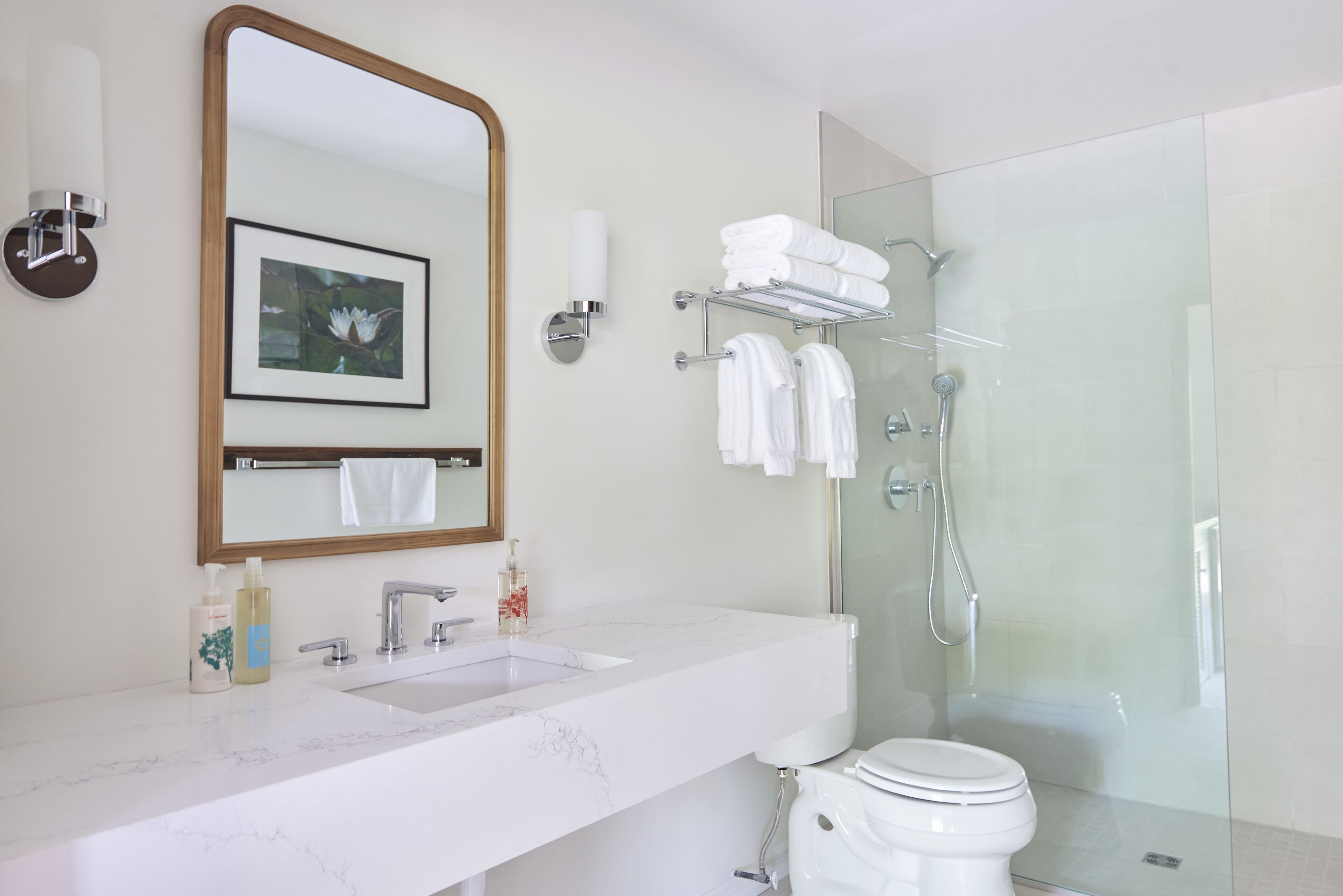 A modern bathroom with a marble sink, a large mirror, a framed picture, and a glass-enclosed shower area.