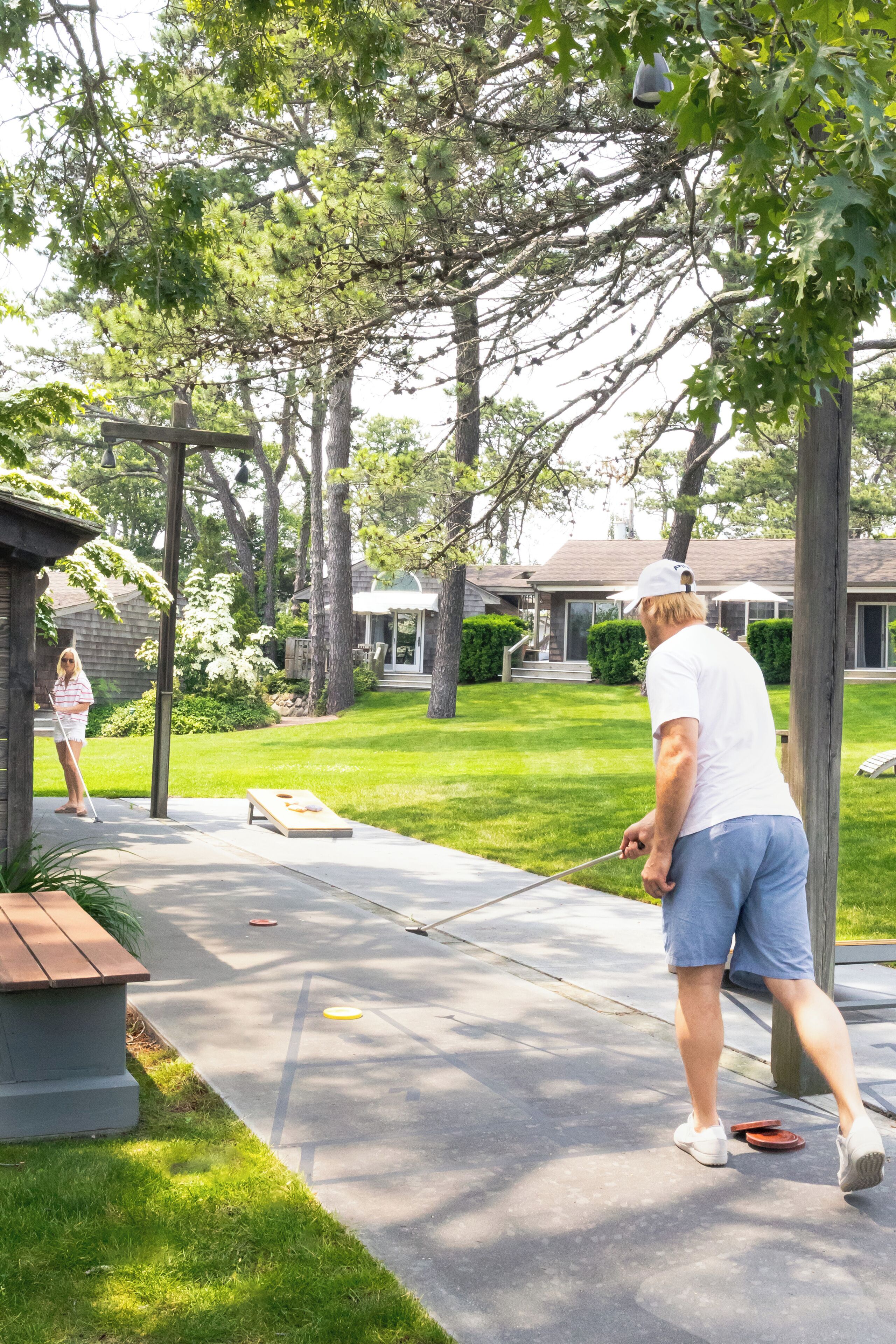 Un cadre résidentiel avec une allée pavée, un banc en bois et une maison dotée d’un porche.