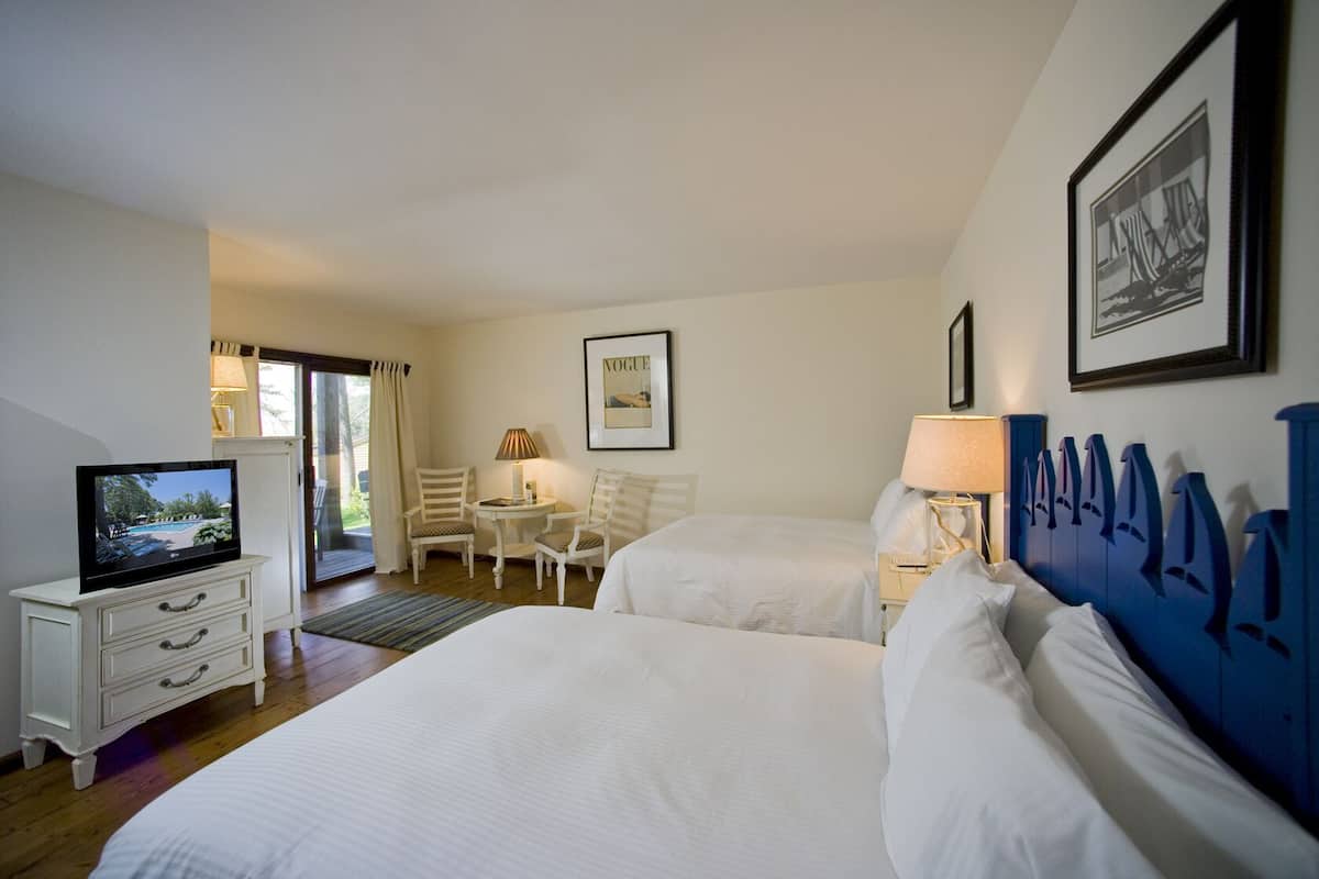 Habitación de hotel con dos camas, televisión, escritorio con lámpara y una silla.