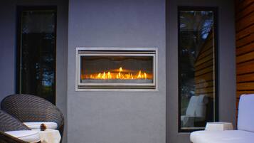 A modern outdoor seating area with a built-in fireplace, wicker chairs, and a white sofa.