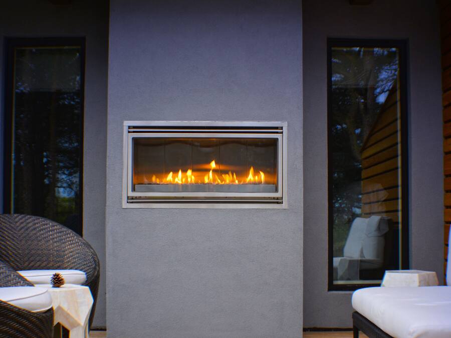 A modern outdoor seating area with a built-in fireplace, wicker chairs, and a white sofa.
