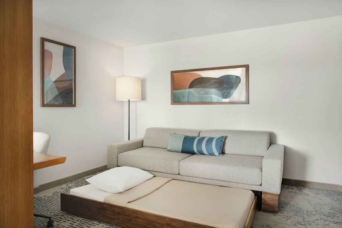 A modern hotel room with a sofa, a bed, a lamp, and abstract wall art.