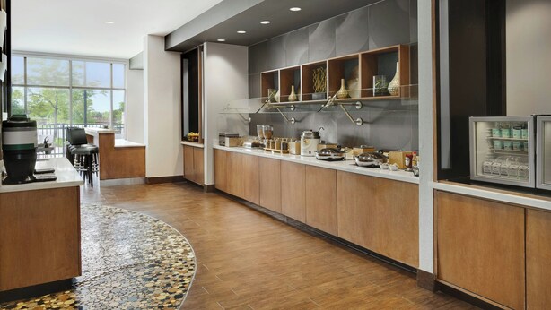 A modern kitchen with wooden cabinets, a glass display case, and a large window providing a view of the outdoors. - SpringHill Suites Chicago Southeast/Munster IN (Munster)