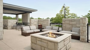 An outdoor patio with stone walls, a fire pit, and multiple seating areas. - SpringHill Suites Chicago Southeast/Munster IN (Munster)