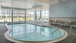 An indoor swimming pool with clear views of the outside, surrounded by lounge chairs and tables. - SpringHill Suites Chicago Southeast/Munster IN (Munster)