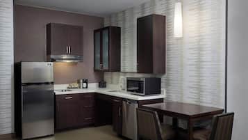 A compact kitchen with dark wooden cabinets, a stainless steel refrigerator, a microwave, and a dishwasher.