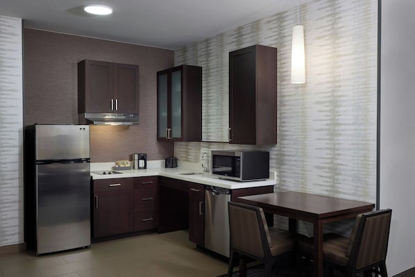 Cocina compacta con armarios de madera oscura, refrigerador de acero inoxidable, microondas y lavavajillas.