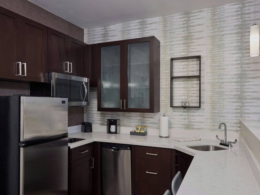 A modern kitchen with dark wood cabinets, stainless steel appliances, a dishwasher, a microwave, and a sink.