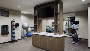 Una sala de fitness amb equips d'exercici, un televisor i un dispensador d'aigua.