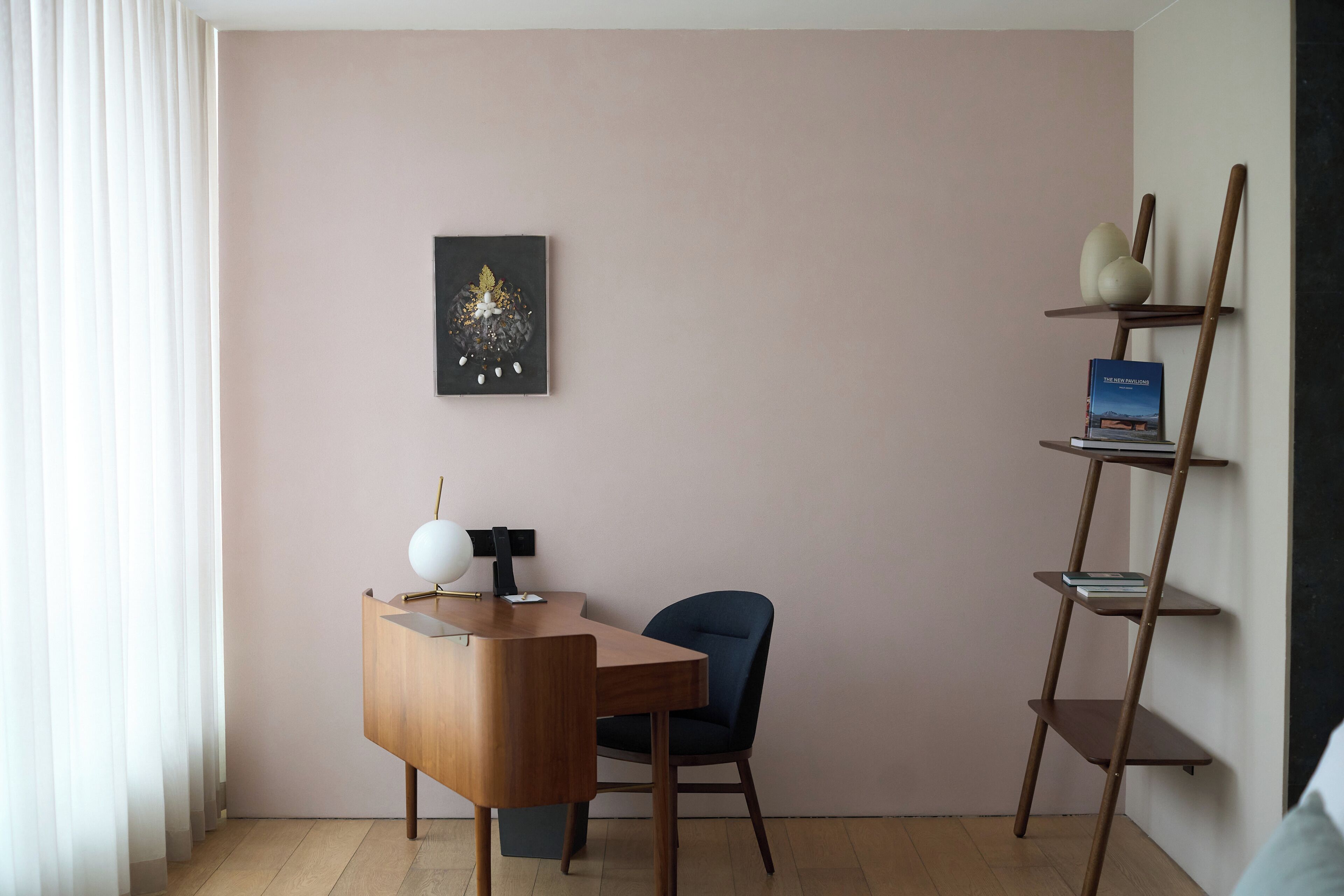 Een moderne kamer met een houten bureau, een blauwe stoel, een wandplank met boeken en een ingelijst kunstwerk.