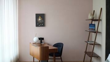 Een moderne kamer met een houten bureau, een blauwe stoel, een wandplank met boeken en een ingelijst kunstwerk.