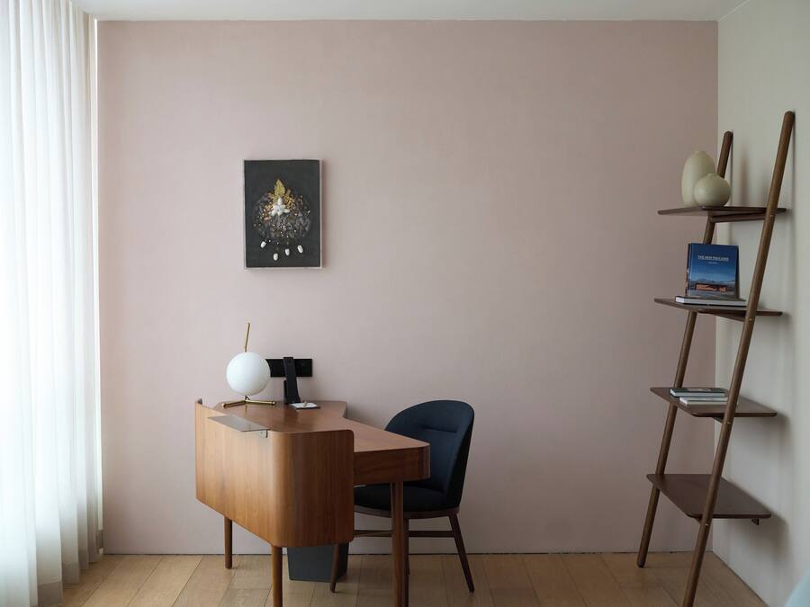 Een moderne kamer met een houten bureau, een blauwe stoel, een wandplank met boeken en een ingelijst kunstwerk.