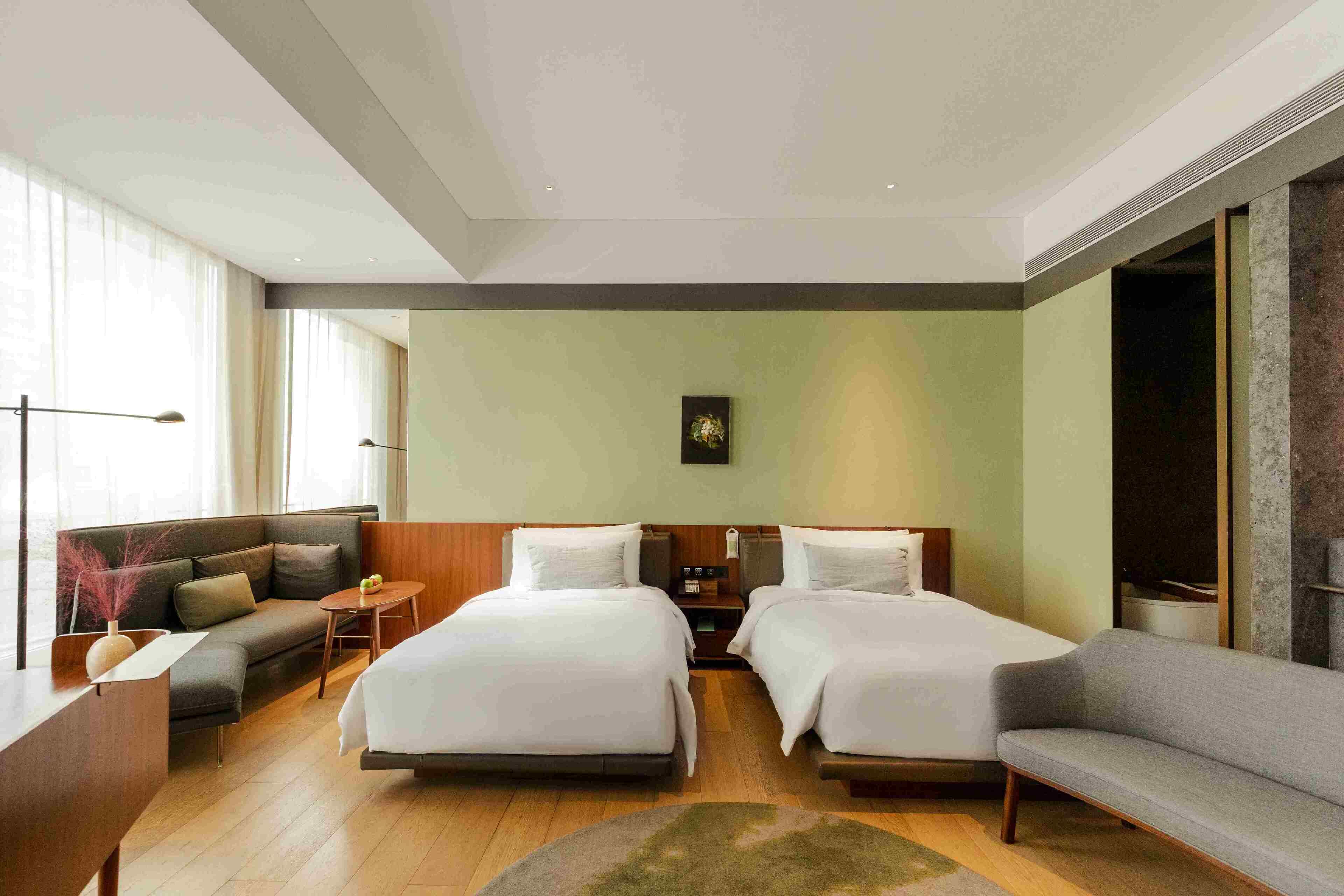 Una habitación de hotel con dos camas, un sofá, un escritorio y un ventanal grande.
