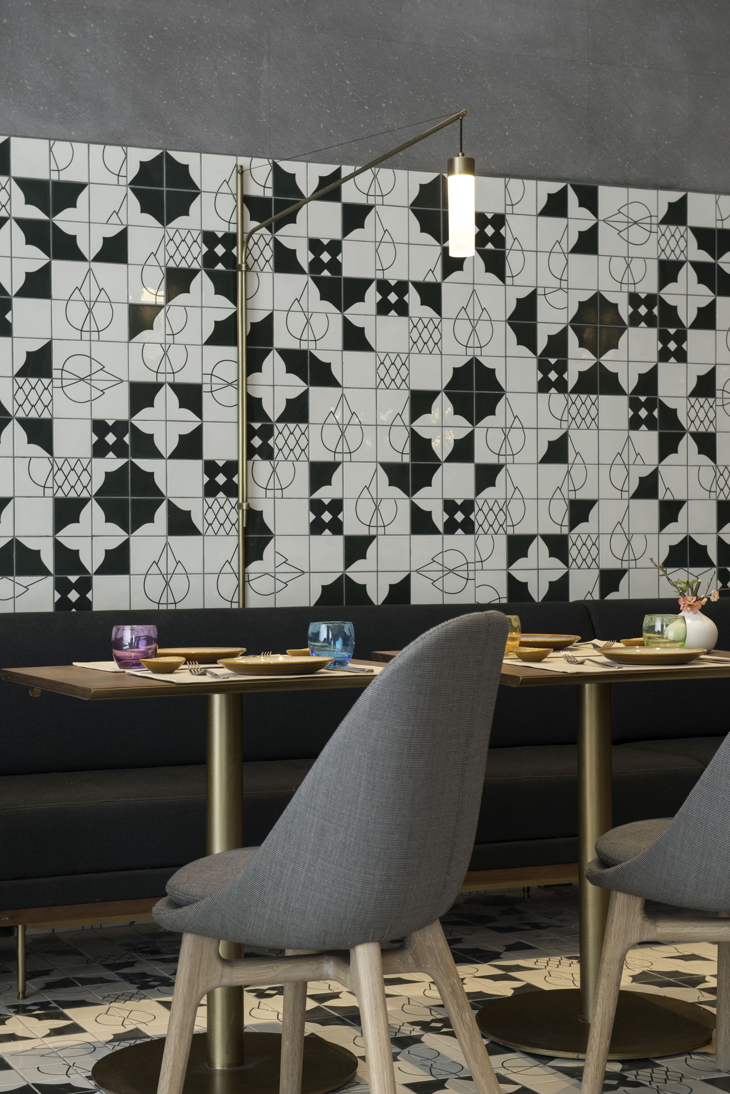 A dining area with a black and white patterned wall, a wooden table, and two grey upholstered chairs.