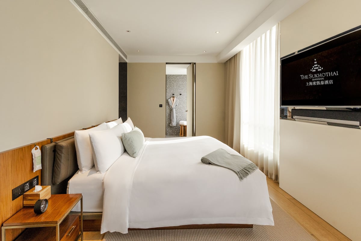 A hotel room with a large bed, a TV on the wall, and a view of the city.