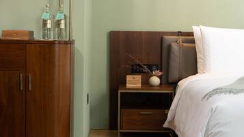 A neatly arranged hotel room with a wooden wardrobe, a bedside table with a vase of dried branches, and a bed with a white pillow and a brown headboard.