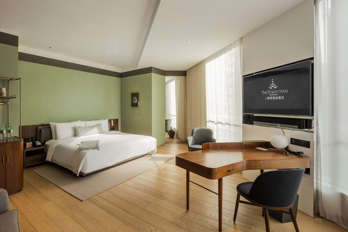 A hotel room with a bed, desk, chair, and a TV displaying hotel branding.