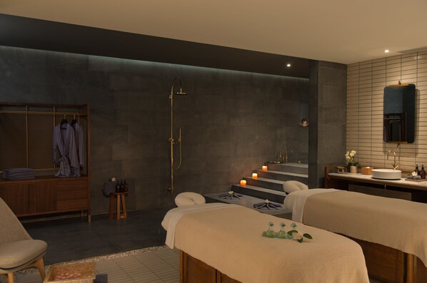 Un spa moderno con una banca de madera, camilla de masaje, zona de ducha y tocador con espejo.