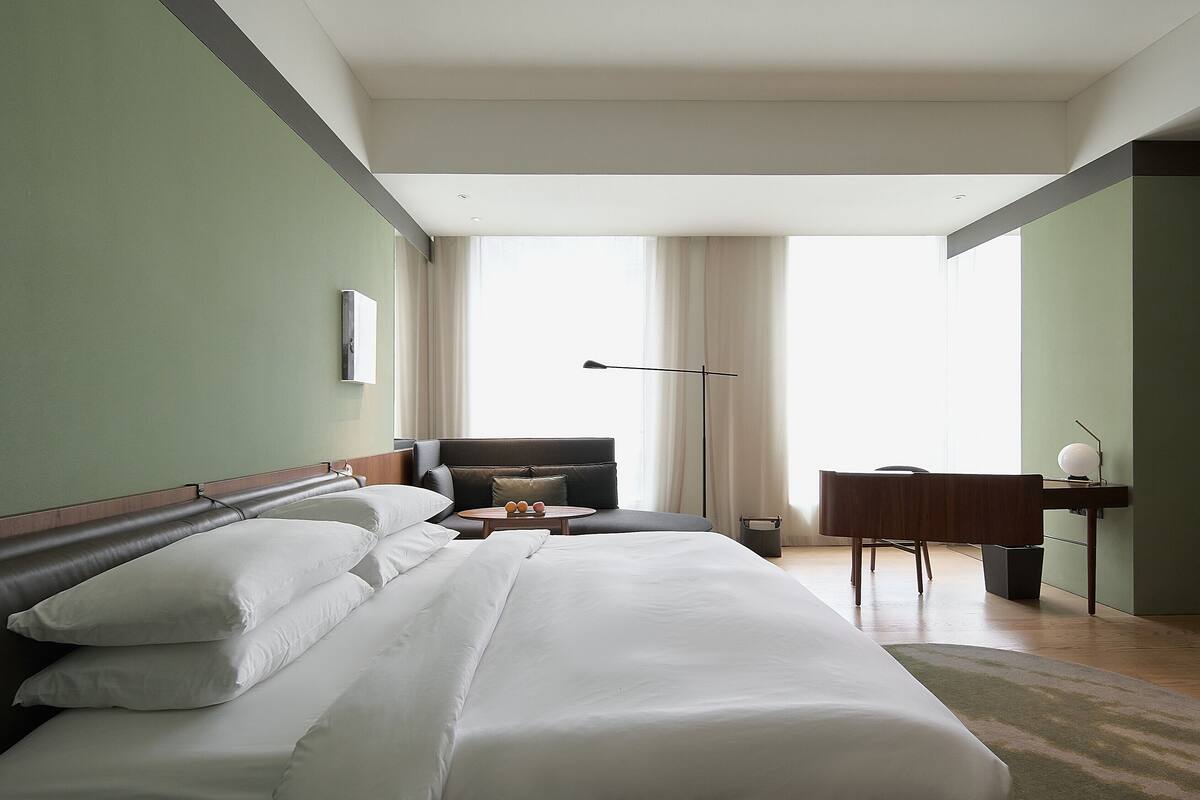 A hotel room with a large bed, a desk, a chair, and a view of the outdoors.