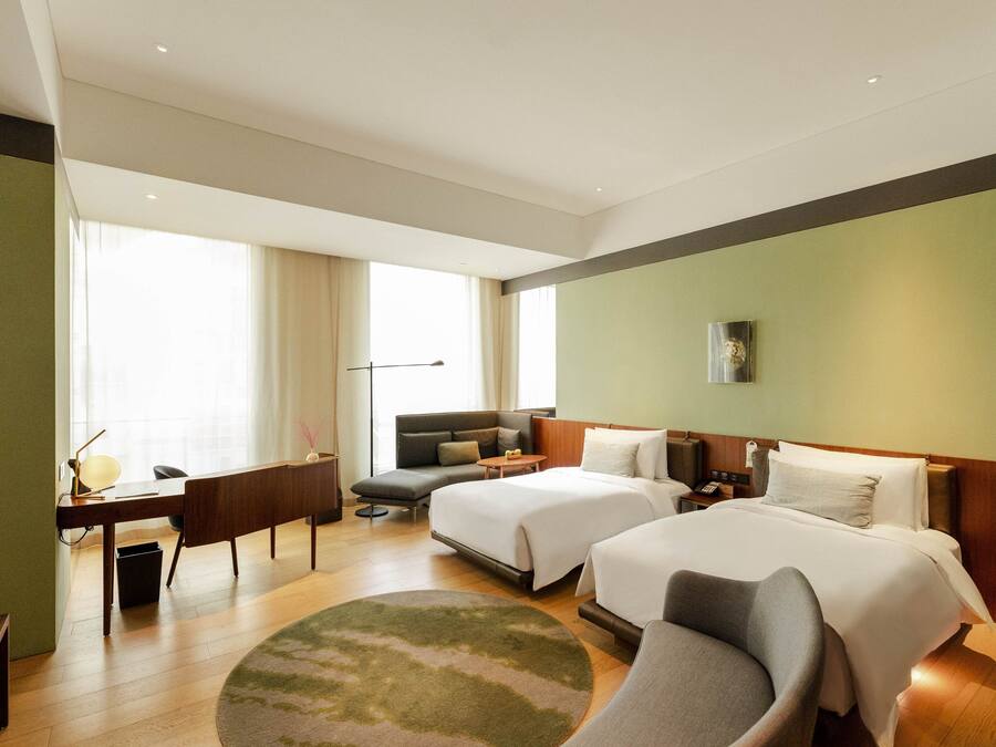 Habitación de hotel con dos camas, un escritorio, un sofá y un ventanal grande.