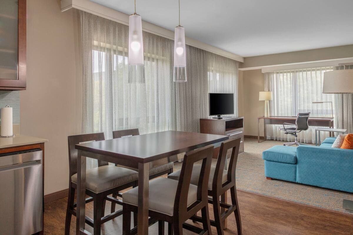Habitación de hotel con comedor, sofá, televisor y escritorio.