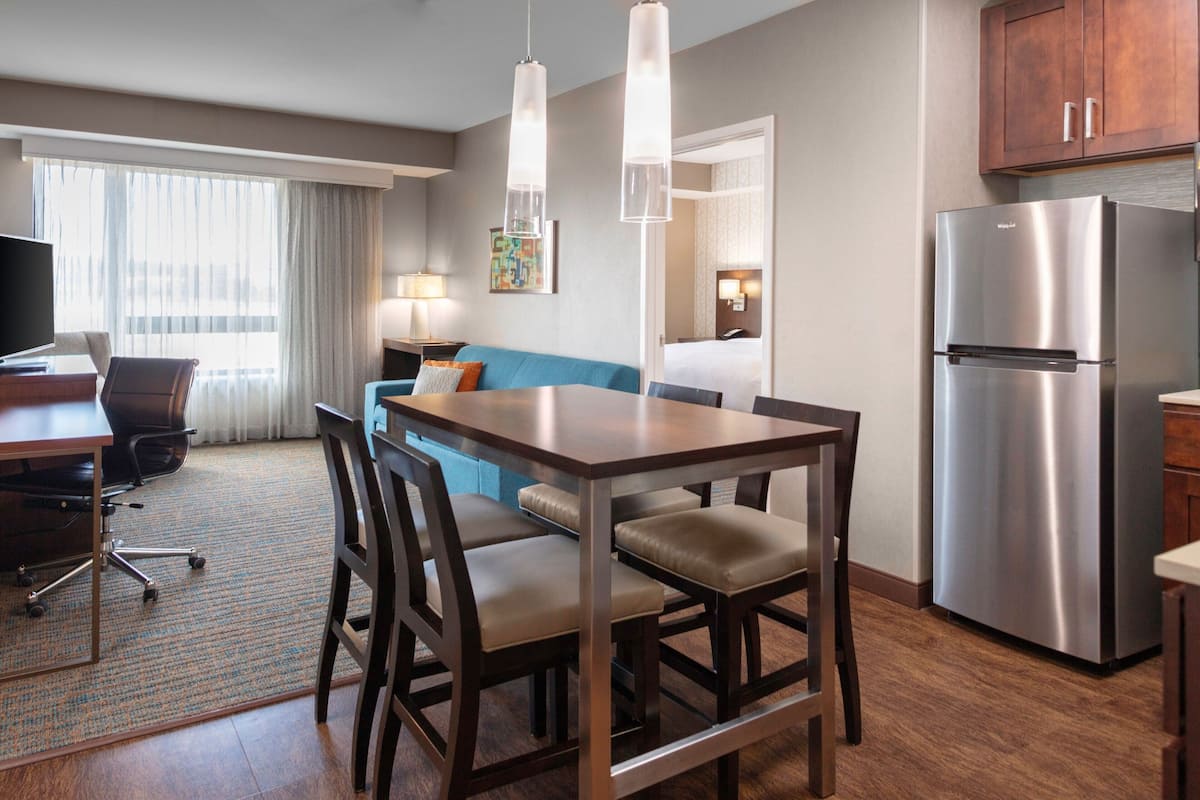 Una habitación de hotel moderna con comedor, kitchenette y sala de estar con sofá y televisor.