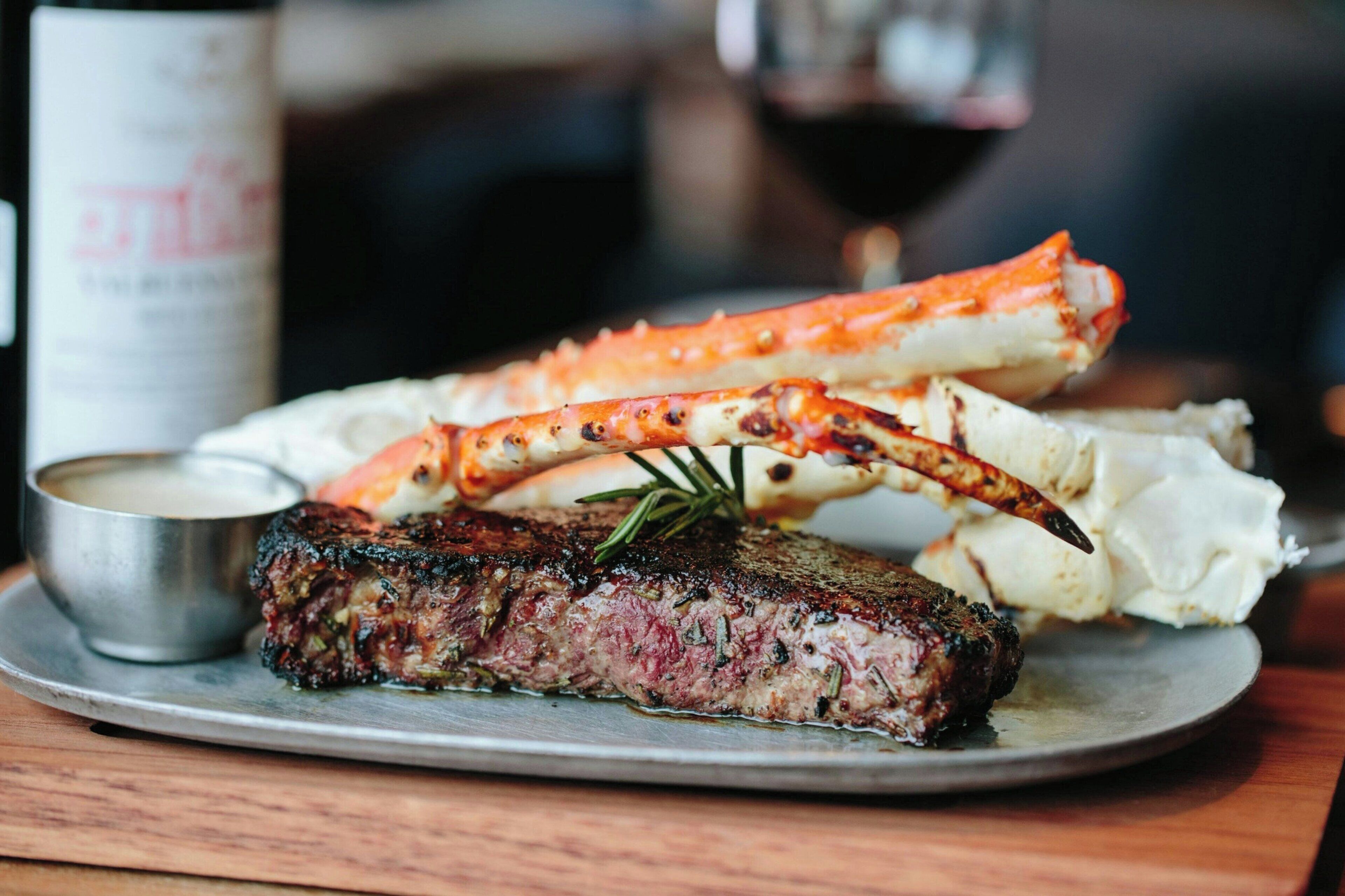 Un steak accompagné d’une queue de homard et d’un petit ramequin de sauce, le tout présenté sur une assiette.