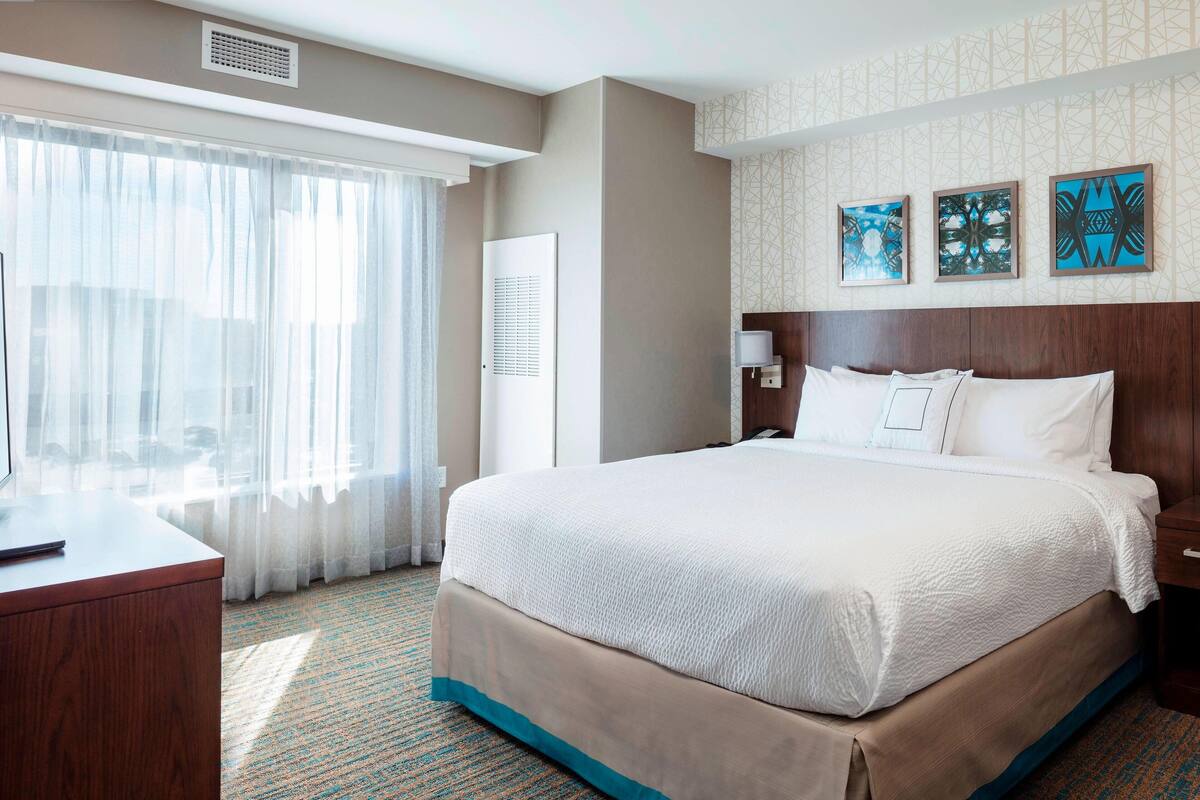 Una habitación de hotel con una cama grande, un escritorio y una ventana con cortinas de gasa.