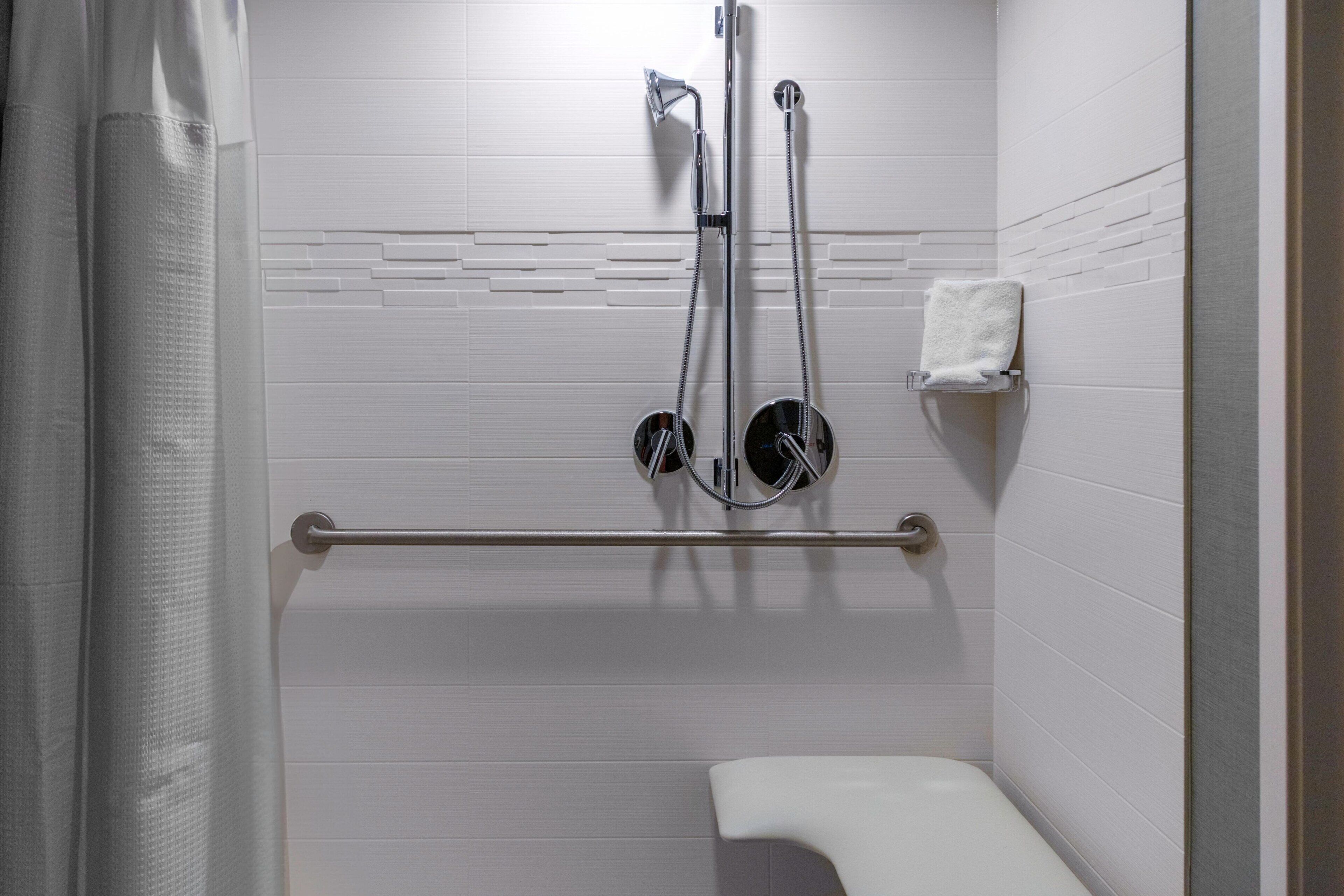 A bathroom with white tiled walls, a white toilet, a grab bar, and a shower head.