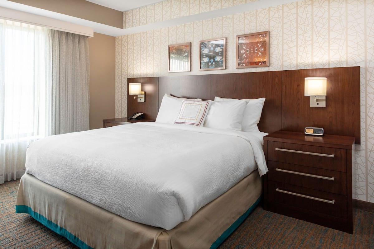 Una habitación de hotel con una cama grande, una mesita de noche con lámpara y un teléfono en la pared.