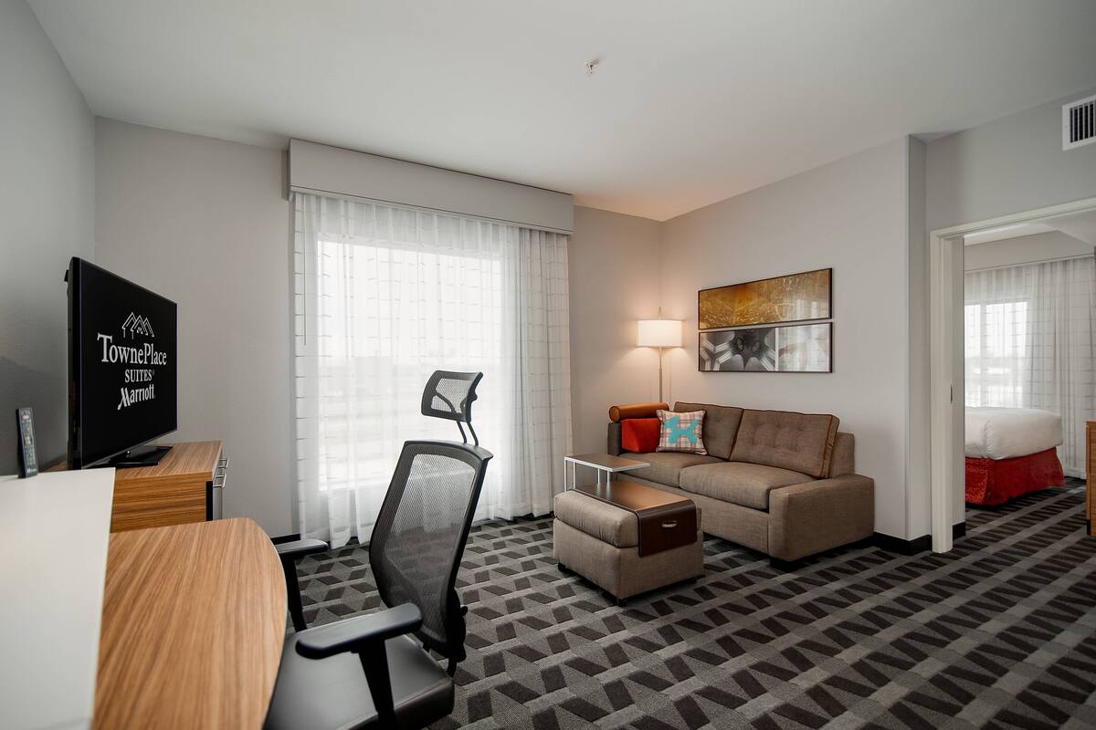 Une chambre d’hôtel équipée d’un canapé, d’un fauteuil, d’un bureau, d’une télévision et d’une lampe.