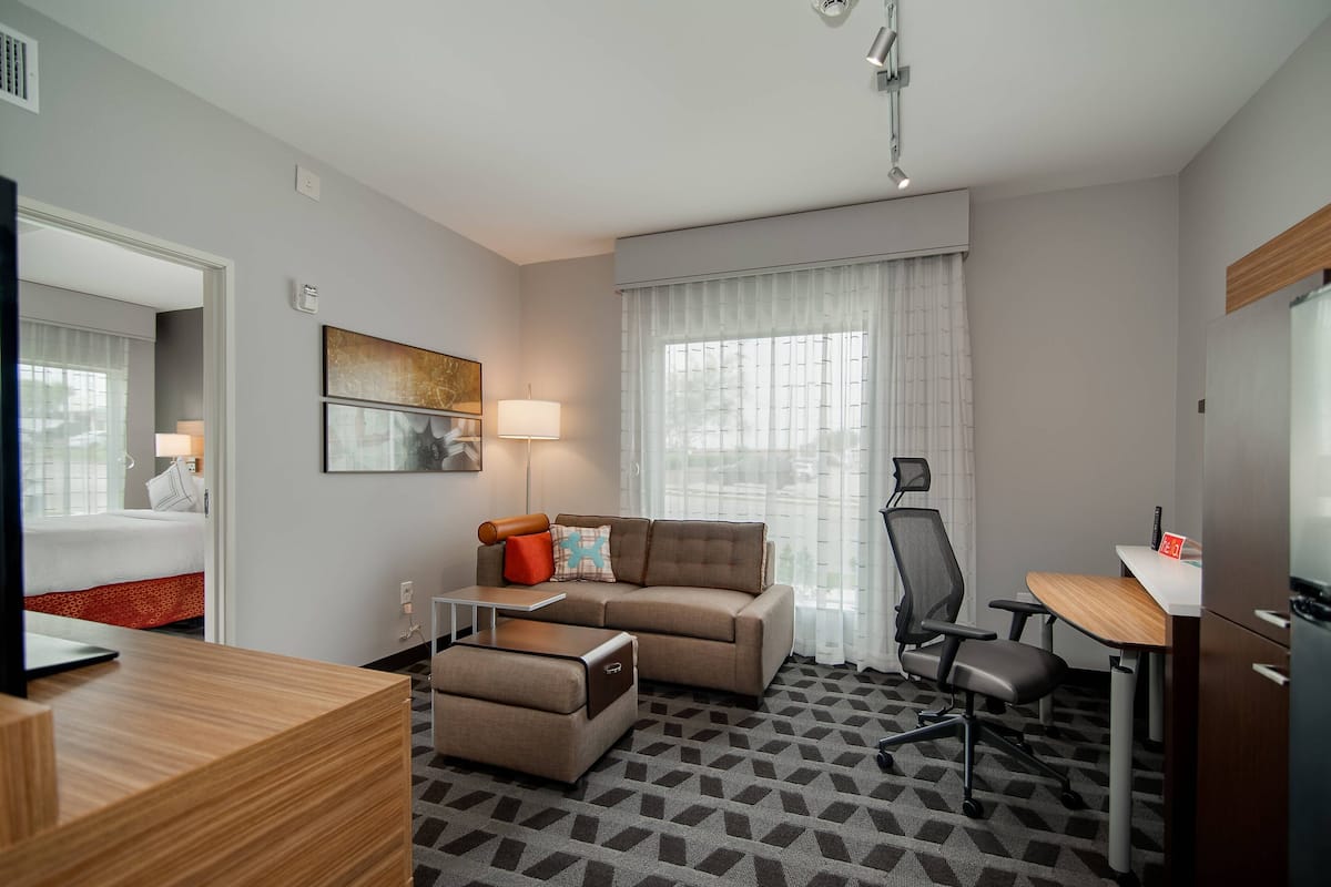 Une chambre d’hôtel avec un canapé, un fauteuil, un bureau et un lit à l’arrière-plan.