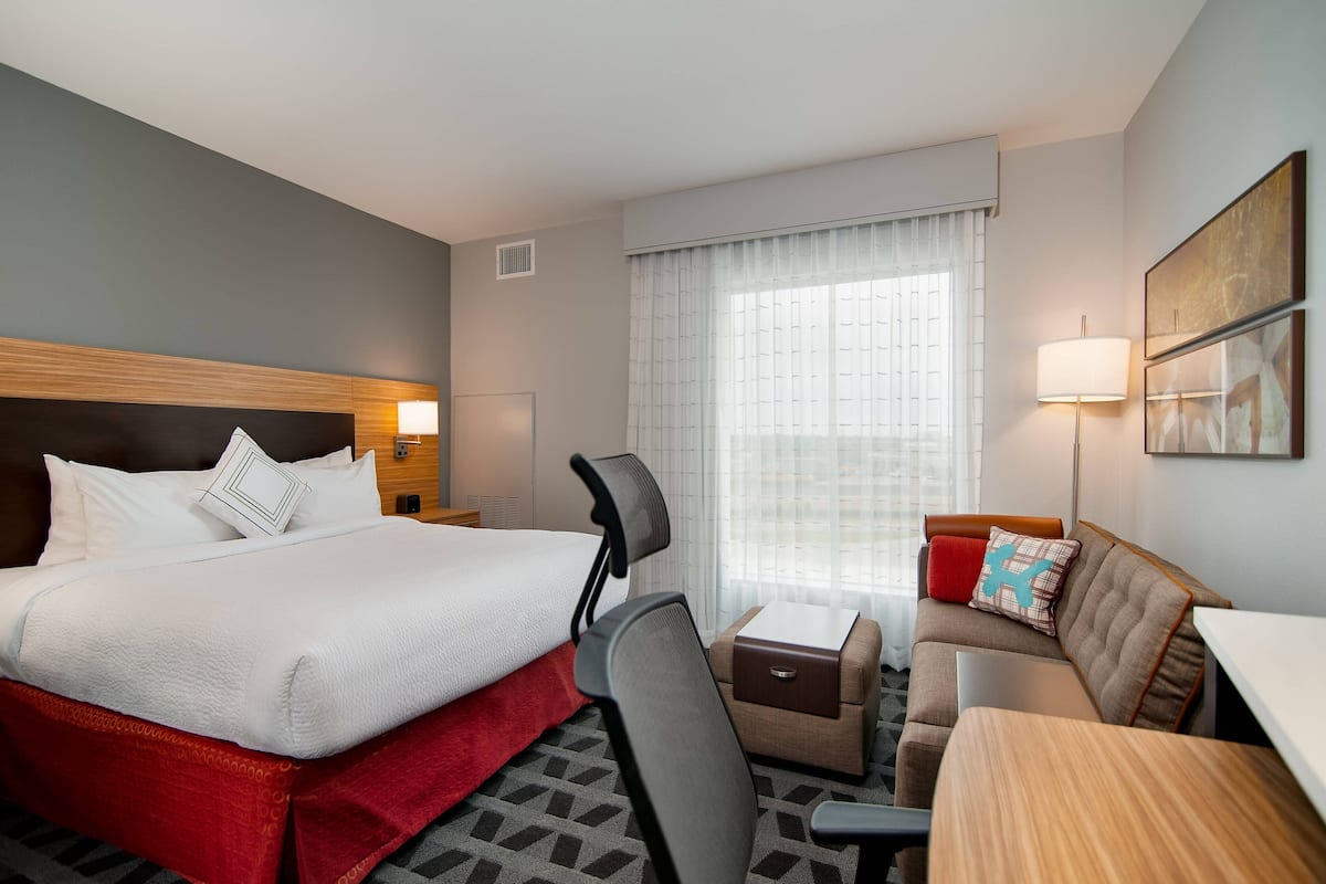 Une chambre d’hôtel avec un lit, un bureau, une chaise, un canapé et une fenêtre avec des rideaux.