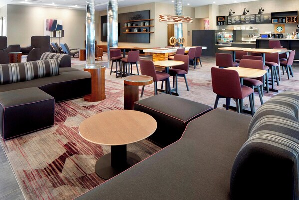 Un moderno vestíbulo de hotel con zonas de estar, un bar y una estación de café.