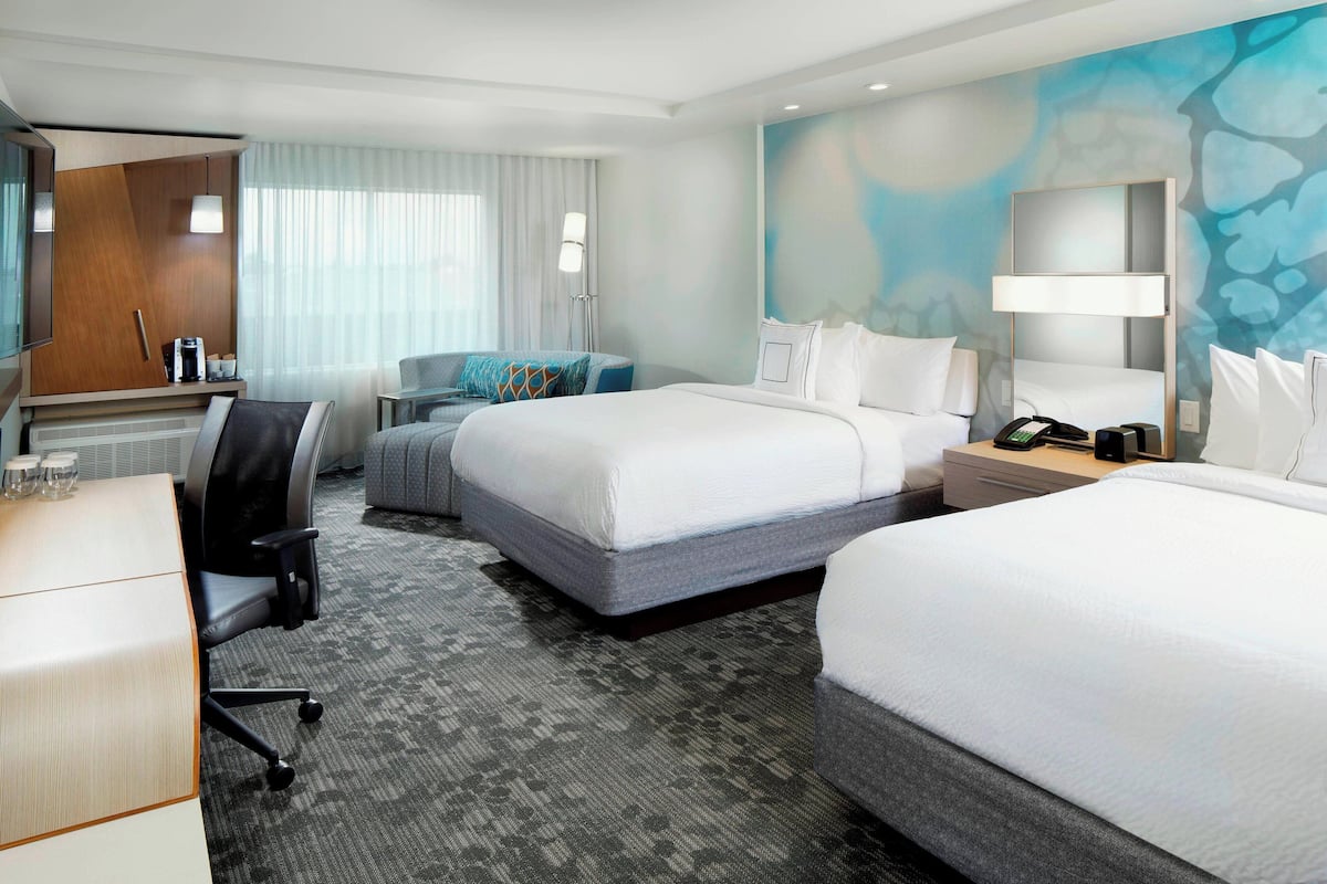 A hotel room with two beds, a desk, a chair, and a couch.