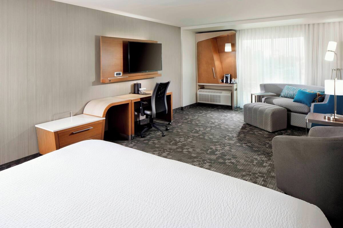 A hotel room with a large bed, a desk with a chair, a sofa, and a TV mounted on the wall.