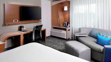 A hotel room with a bed, a desk, a TV, a sofa, and a window with curtains.
