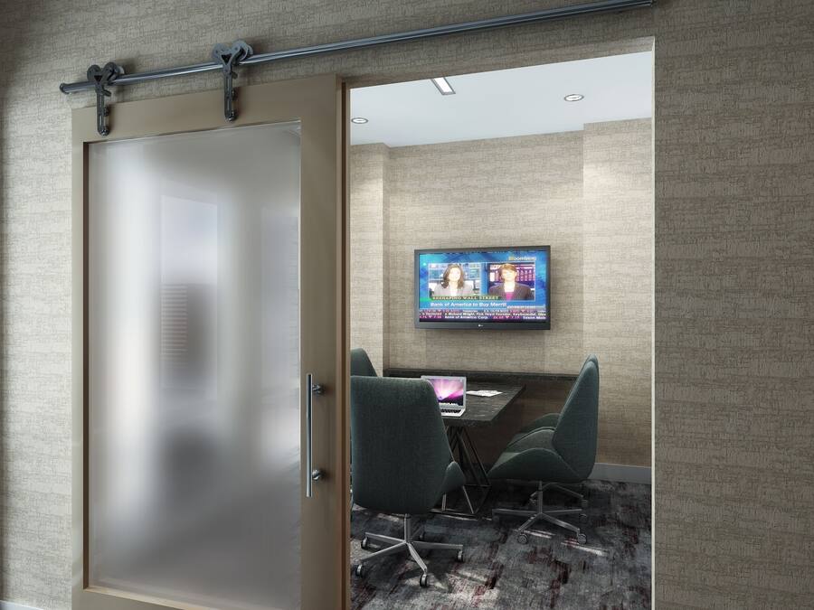 A modern conference room with a large screen displaying Bloomberg, a glass door, and a carpeted floor.