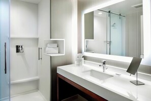 Un baño moderno con un espejo grande, un lavamanos blanco y una cabina de ducha de vidrio.