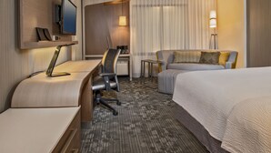 Ein Hotelzimmer mit Schreibtisch, Stuhl, Bett und einem an der Wand montierten Fernseher.