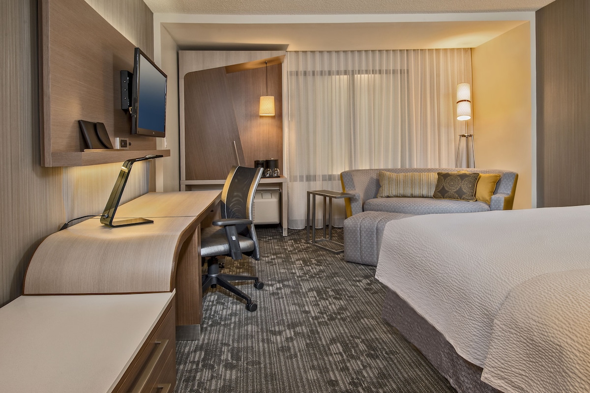 Ein Hotelzimmer mit Schreibtisch, Stuhl, Bett und einem an der Wand montierten Fernseher.