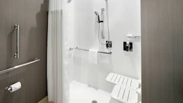 A modern bathroom with a shower, toilet, and handrails.