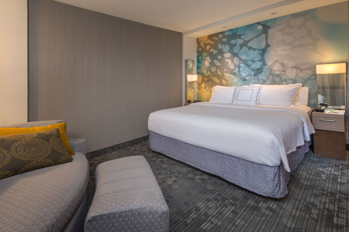 A hotel room with a large bed, a sofa, a small table, and a wall with a textured pattern.