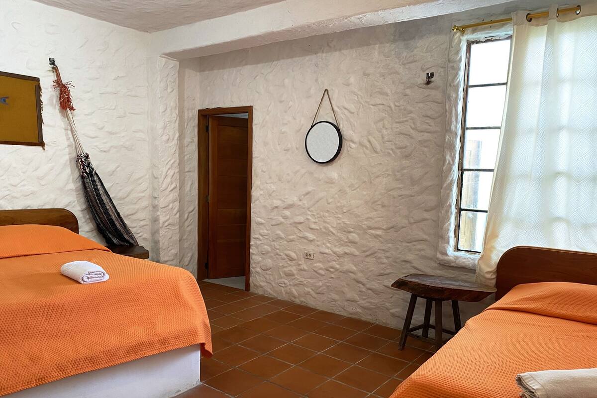 A room with two beds, a small table, a mirror, and a window with curtains.