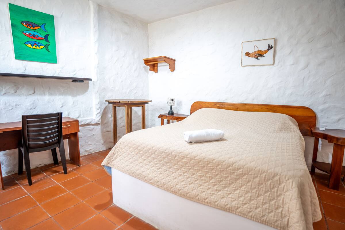 A bedroom with a bed, a desk, a chair, and a small table.