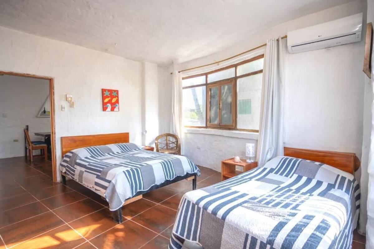 A room with two beds, a window with curtains, a chair, and an air conditioning unit.