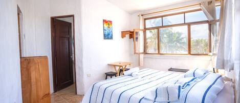 Un dormitorio con una cama, un armario de madera, una mesita pequeña y una ventana con cortinas.