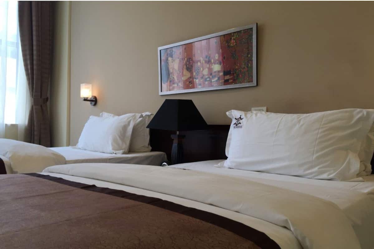A hotel room with two beds, a painting on the wall, a lamp, and a window with curtains.